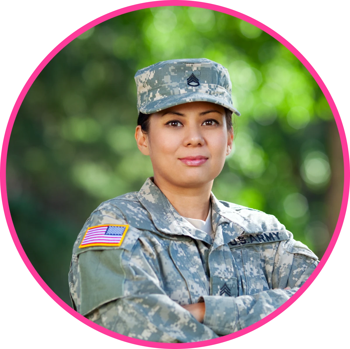 A person in a U.S. Army uniform stands outdoors with arms crossed, wearing a camouflage cap and displaying a patch of the American flag on their sleeve.